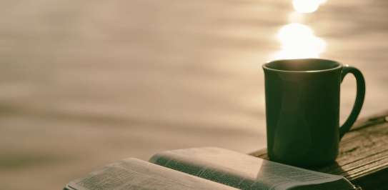 A bible and cup of tea next to a large body of water