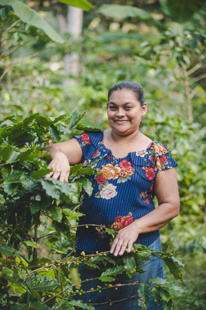 Angela clasping a coffee plant smiling 