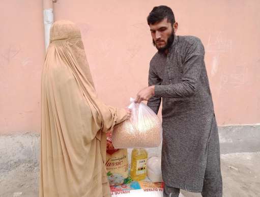 A woman, left, in full cover recieves emergency food supplies from a young man on the right