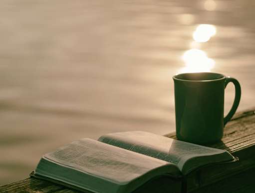 A bible and cup of tea next to a large body of water