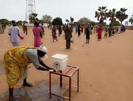 A man using a hand washing station set up by SPEDP with other members of the community standing in designated socially distant circles