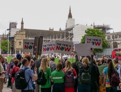 London, 2019. A group of people standing by the Houses of Parliament hold banners saying 'the time is now'