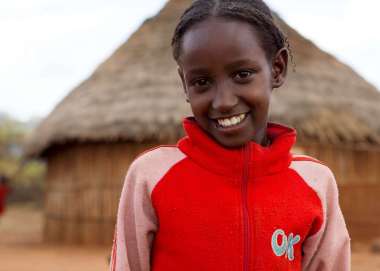 Ten-year-old Negele Dhiba stands in front of a house in her village in Ethiopia